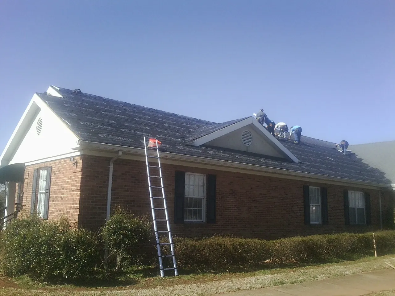 Crew tearing shingles off a brick ranch roof with a ladder set — Emergency Roof Repair work by our crew in Kansasville