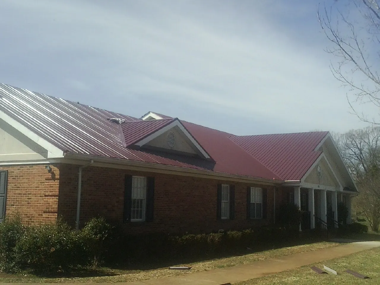 Red metal roof with gabled entries on a long brick building, from a Hail Damage Roof Repair job in Kansasville
