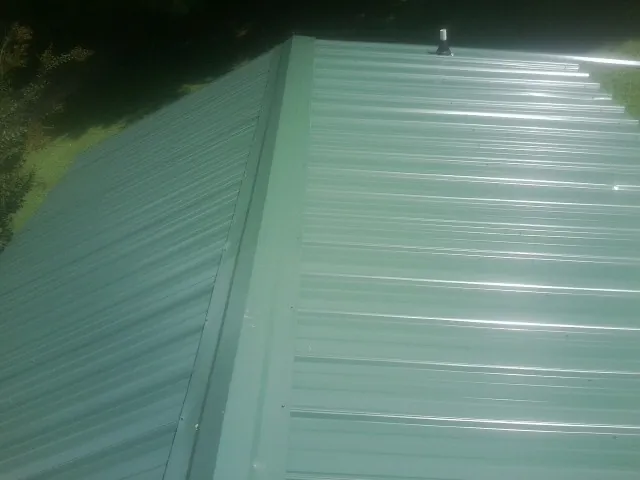 New green metal panels meeting at the ridge of a roof — Flat Roof Repair work by our crew in Kansasville