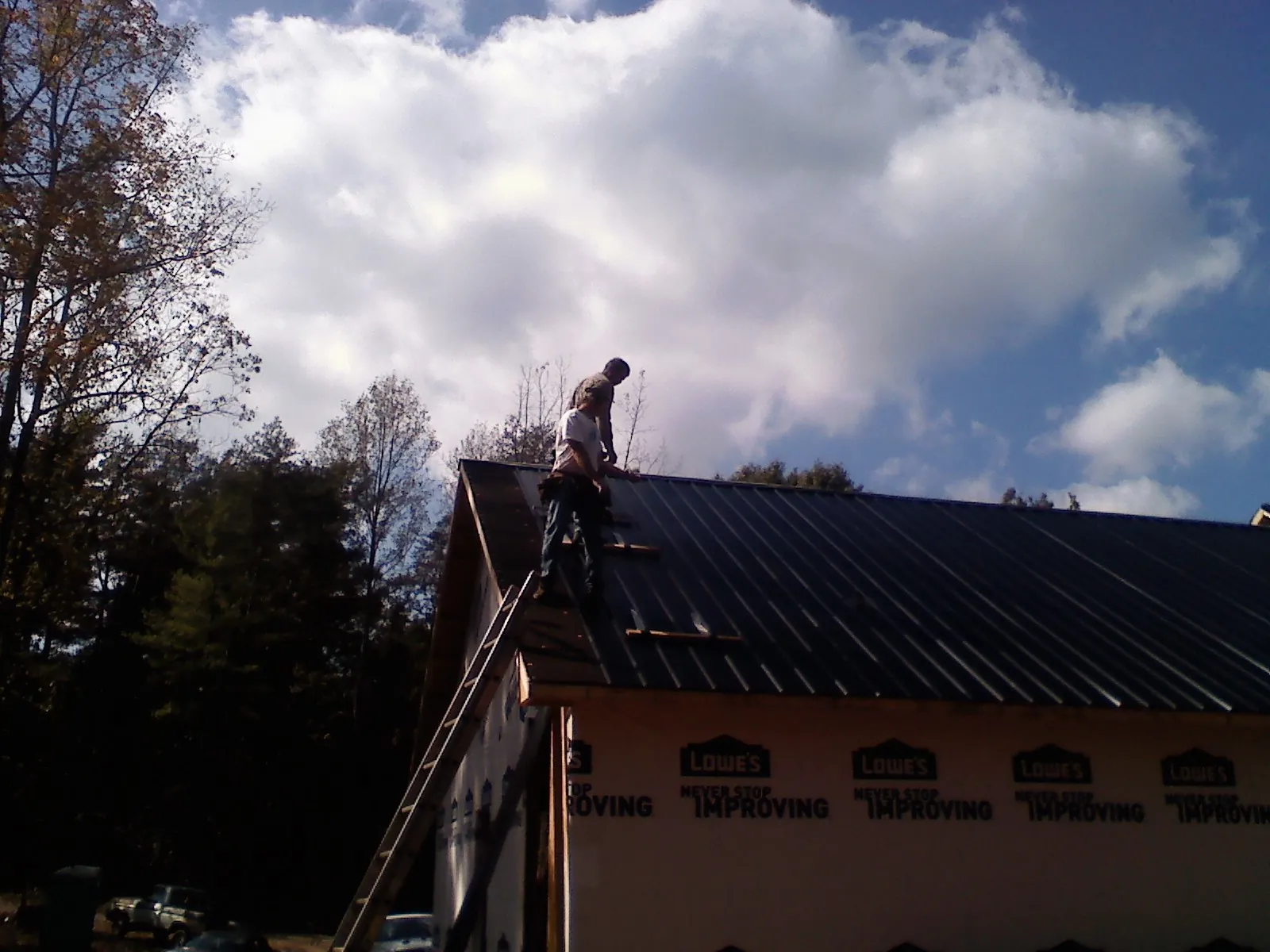 Roofer fastening dark metal panels high against a cloudy sky, from a Roof Inspection job in Kansasville