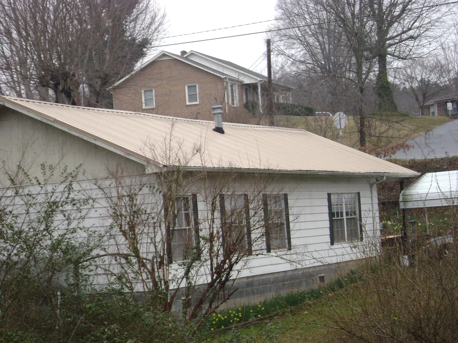 Tan metal roof on a white sided house set into a hillside — Commercial Roofing by Roofing Brothers in Kansasville